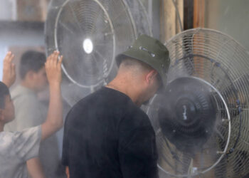 An Iraqi boy and man cool off they stand in front of 'water spray fans' placed on the sidewalk as temperatures soar on Al-Sinak street in central Baghdad amid rising temperatures on June 29, 2025. (Photo by AHMAD AL-RUBAYE / AFP)